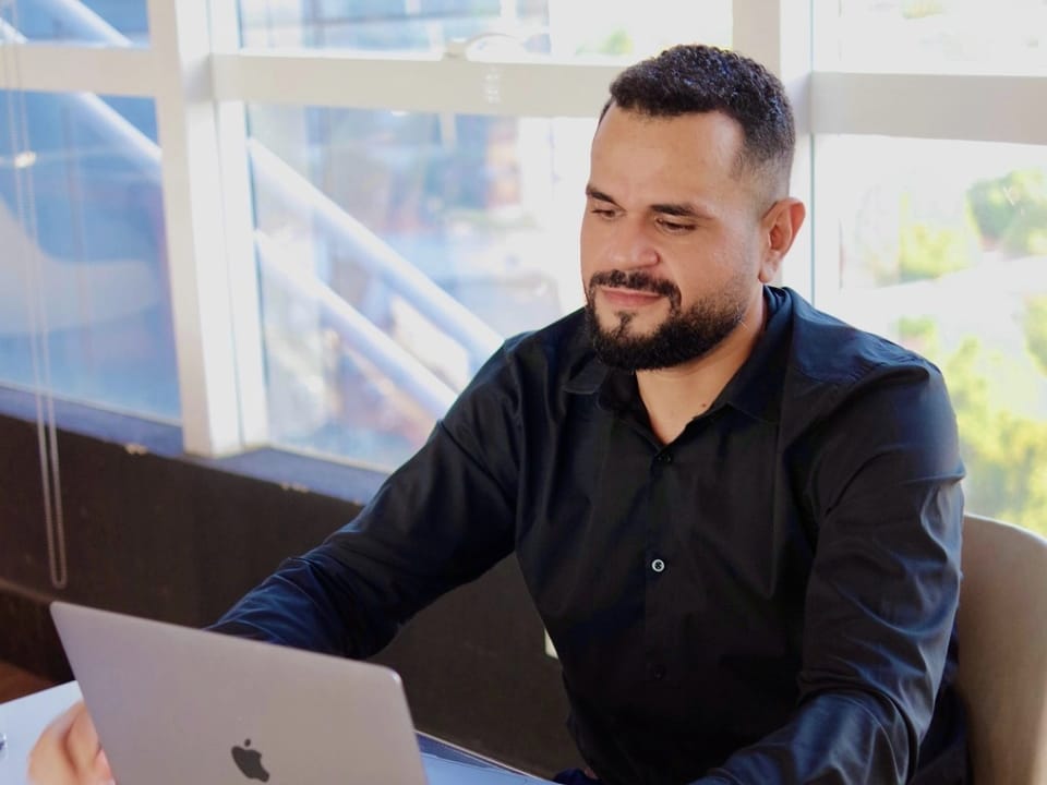 José Ferreira Neto, fundador da Projeta Partners, trabalhando no notebook em um escritório com vista para a cidade